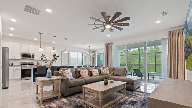 A modern living room with a sofa, coffee table, and a ceiling fan. - Stunning Modern Home! (Kissimmee)