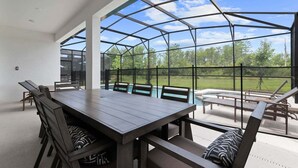 A covered patio with a dining table and chairs, a pool, and a view of the outdoors. - Stunning Modern Home! (Kissimmee)