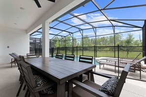 A covered patio with a dining table and chairs, a pool, and a view of the outdoors.