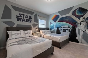 A bedroom with two beds, Star Wars-themed wall art, and a Star Wars-themed bedspread.