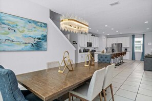 Cozinha moderna com armários brancos, área de jantar com mesa e cadeiras de madeira e um quadro abstrato grande na parede.