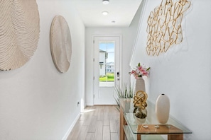 A hallway with a wooden floor, a glass table with decorative items, and a door leading outside.