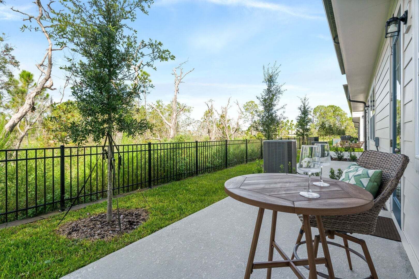 A patio with a round table and chairs, a small tree, and a black metal fence.