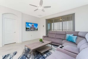 Uma sala de estar moderna com sofá, mesa de centro, ventilador de teto, televisão e janela com persianas.