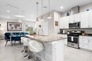 A modern kitchen with white cabinets, a granite countertop, stainless steel appliances, and a dining area with blue chairs.