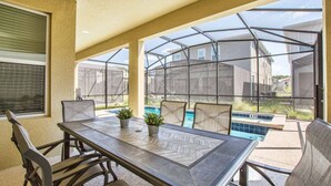 A covered patio with a table and chairs, a pool, and a view of neighboring houses.