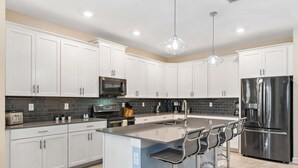 A modern kitchen with white cabinets, stainless steel appliances, a central island with bar stools, and pendant lighting.