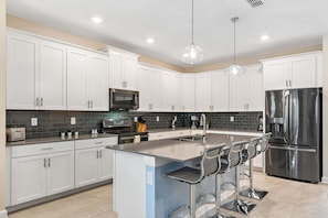A modern kitchen with white cabinets, a stainless steel refrigerator, a microwave, and a coffee maker.