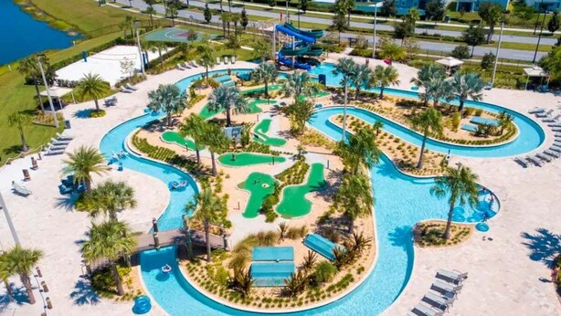 An aerial view of a resort with a large swimming pool, multiple water slides, and a golf course.