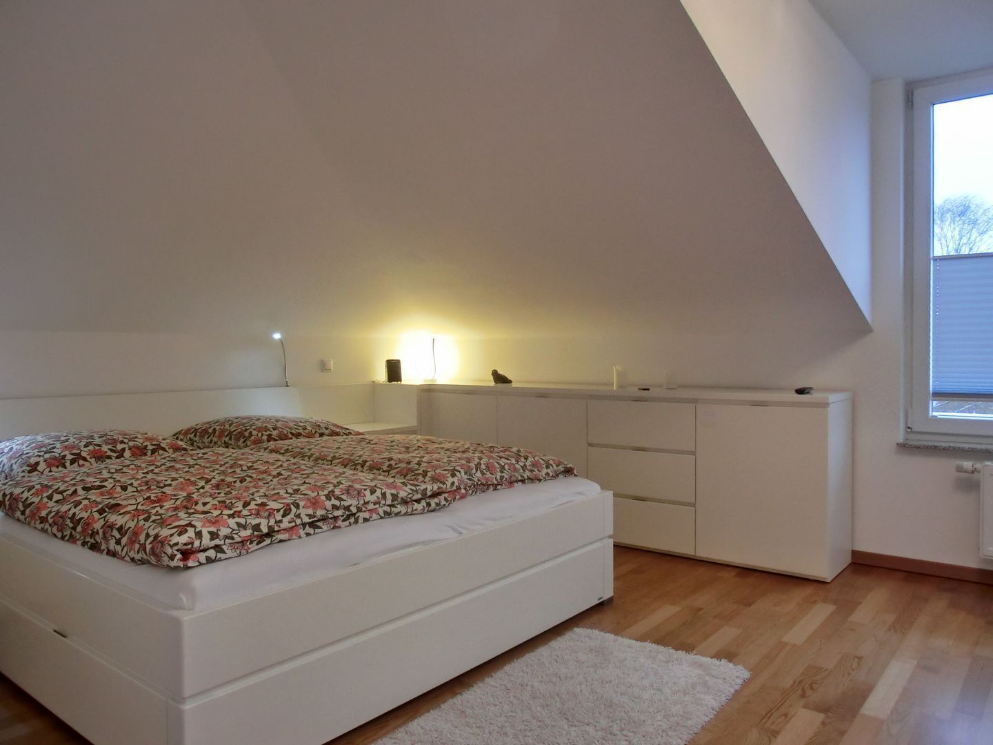 A bedroom with a bed, a desk, and a window.