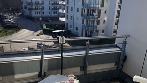 Un balcón con una mesa, dos sillas y vistas a edificios al fondo.