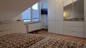 Un dormitorio con techo inclinado, una cama con ropa de cama floral, un armario y un televisor en la pared.