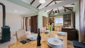 A dining area with a wooden table set for four, a bottle of wine, and a vase with flowers. There is a bookshelf filled with books in the background. - Gorgeous home in Zaboric with private swimming pool, can be inside or outside (Zaboric)