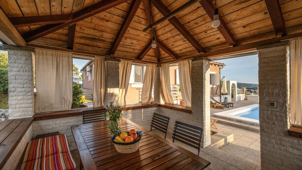 A covered outdoor seating area with a wooden table, chairs, and a fruit basket. - Gorgeous home in Zaboric with private swimming pool, can be inside or outside (Zaboric)