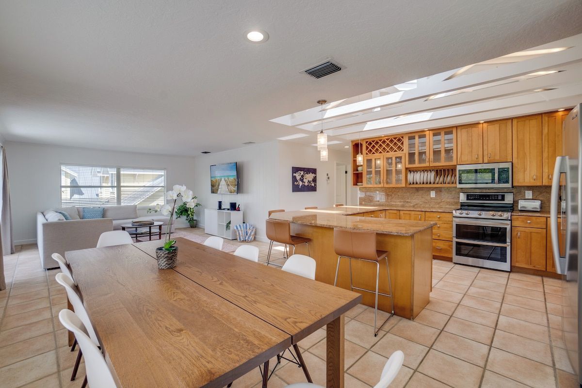 A modern kitchen with a dining area, featuring a wooden table and chairs, a built-in oven, and a kitchen island with bar stools.