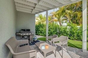 An outdoor patio with a grill, seating, and a view of a well-maintained garden.