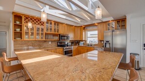 Une cuisine moderne dotée de plans de travail en granit, d’armoires en bois, d’appareils électroménagers en acier inoxydable et d’un grand îlot central avec des tabourets de bar.