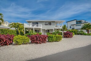 A two-story house with a balcony, surrounded by landscaped gardens and a gravel driveway. - Bean Point Residence Unit A (Anna Maria)
