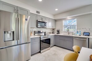 A modern kitchen with stainless steel appliances, grey cabinets, and a window providing natural light.