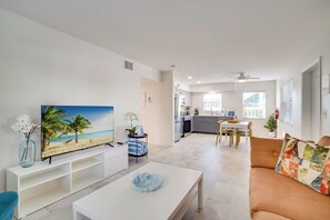 A modern living room with a flat-screen TV, a white coffee table, and a sofa with a colorful cushion.