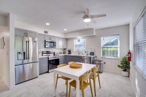 A modern kitchen with stainless steel appliances, a white dining table, and a ceiling fan.
