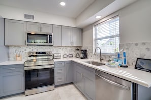 A modern kitchen with grey cabinets, stainless steel appliances, and a window providing natural light. - Bean Point Residence Unit B (Anna Maria)