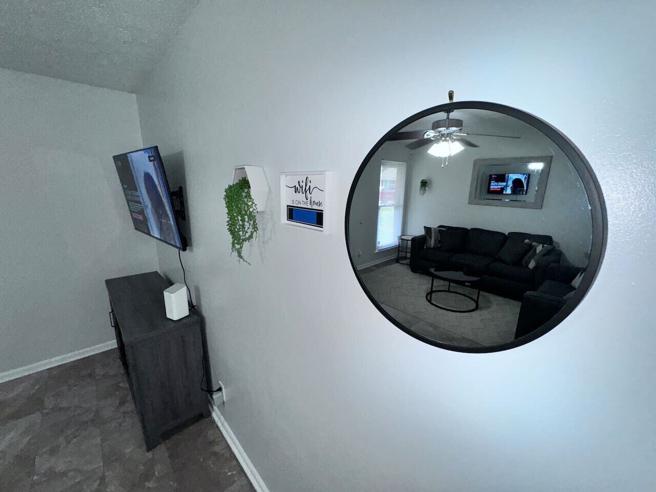 A living room with a round mirror, a flat-screen TV, a small plant, and a sign on the wall.