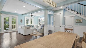 A spacious living room with a large wooden table, a sofa, and a television. There is a staircase leading to another level. - FREE Brand new 6-Seat Golf Cart, Bikes! Somervilla at Naturewalk!!!  Pickleball Courts, Heated Pool! (Santa Rosa Beach)