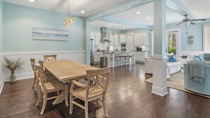 A spacious dining area with a wooden table and chairs, a kitchen in the background, and a view of the outdoors. - FREE Brand new 6-Seat Golf Cart, Bikes! Somervilla at Naturewalk!!!  Pickleball Courts, Heated Pool! (Santa Rosa Beach)