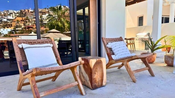 Due poltrone in legno con cuscini, posizionate su un patio piastrellato con vista su una zona residenziale.