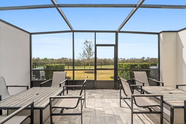 A covered outdoor patio with a view of a landscaped garden and a tree.