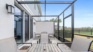 Une terrasse extérieure couverte, avec une table en bois et quatre chaises, de grandes fenêtres et une vue sur les environs.