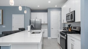 Une cuisine moderne avec des armoires blanches, des appareils en acier inoxydable et des luminaires suspendus.