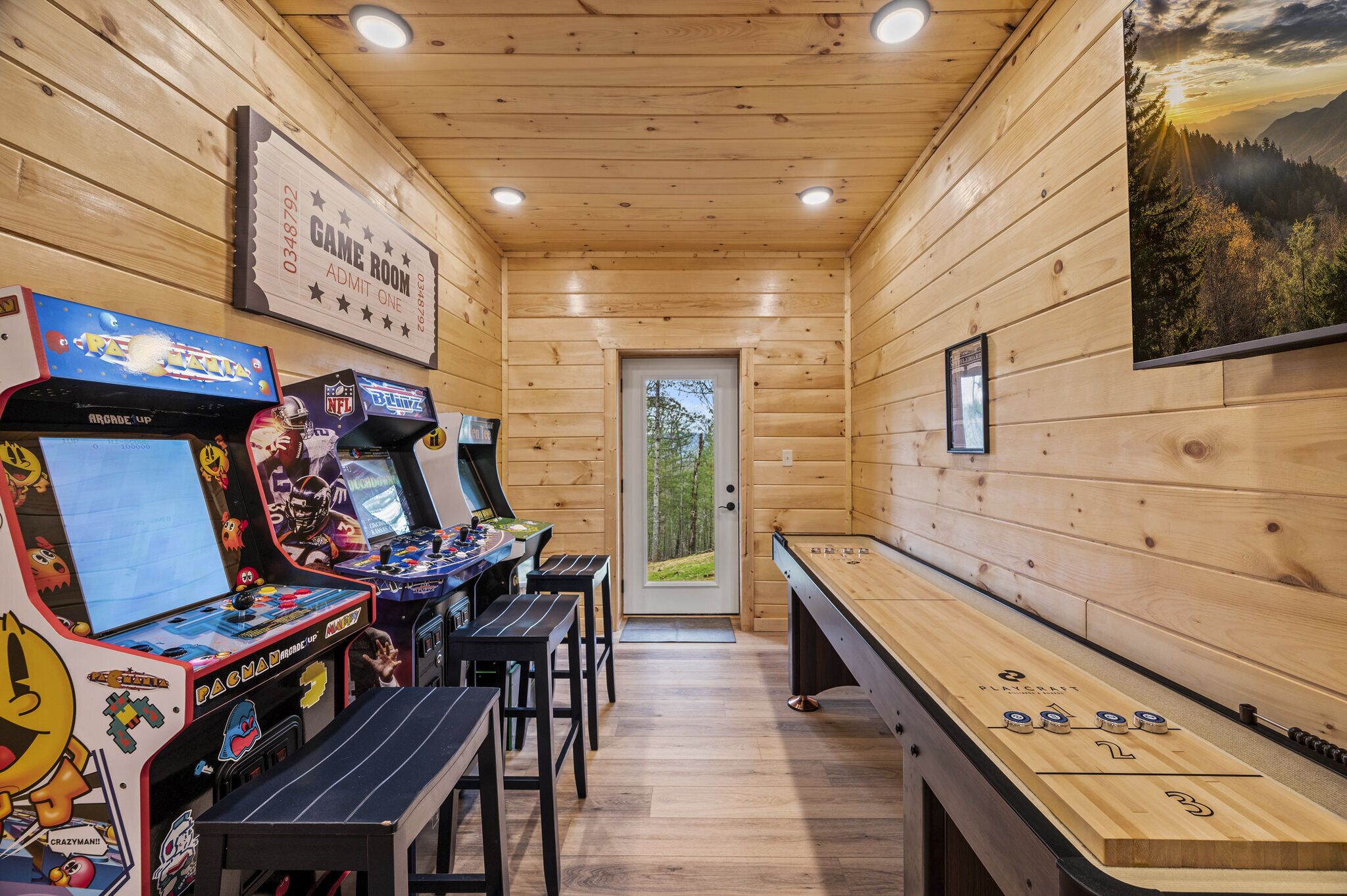A wooden interior with arcade games, a pool table, and a door leading outside.