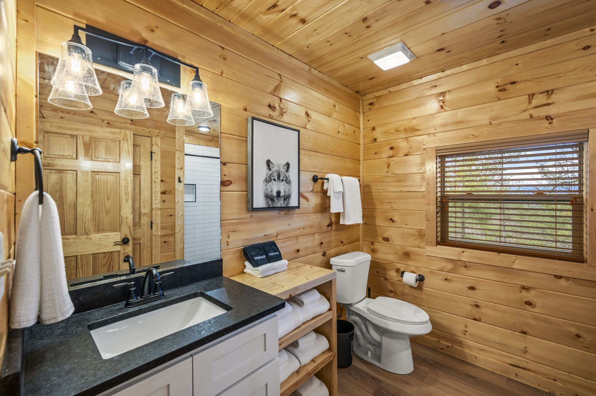 Un bagno in una baita di legno, con lavandino, water e una cornice appesa al muro.
