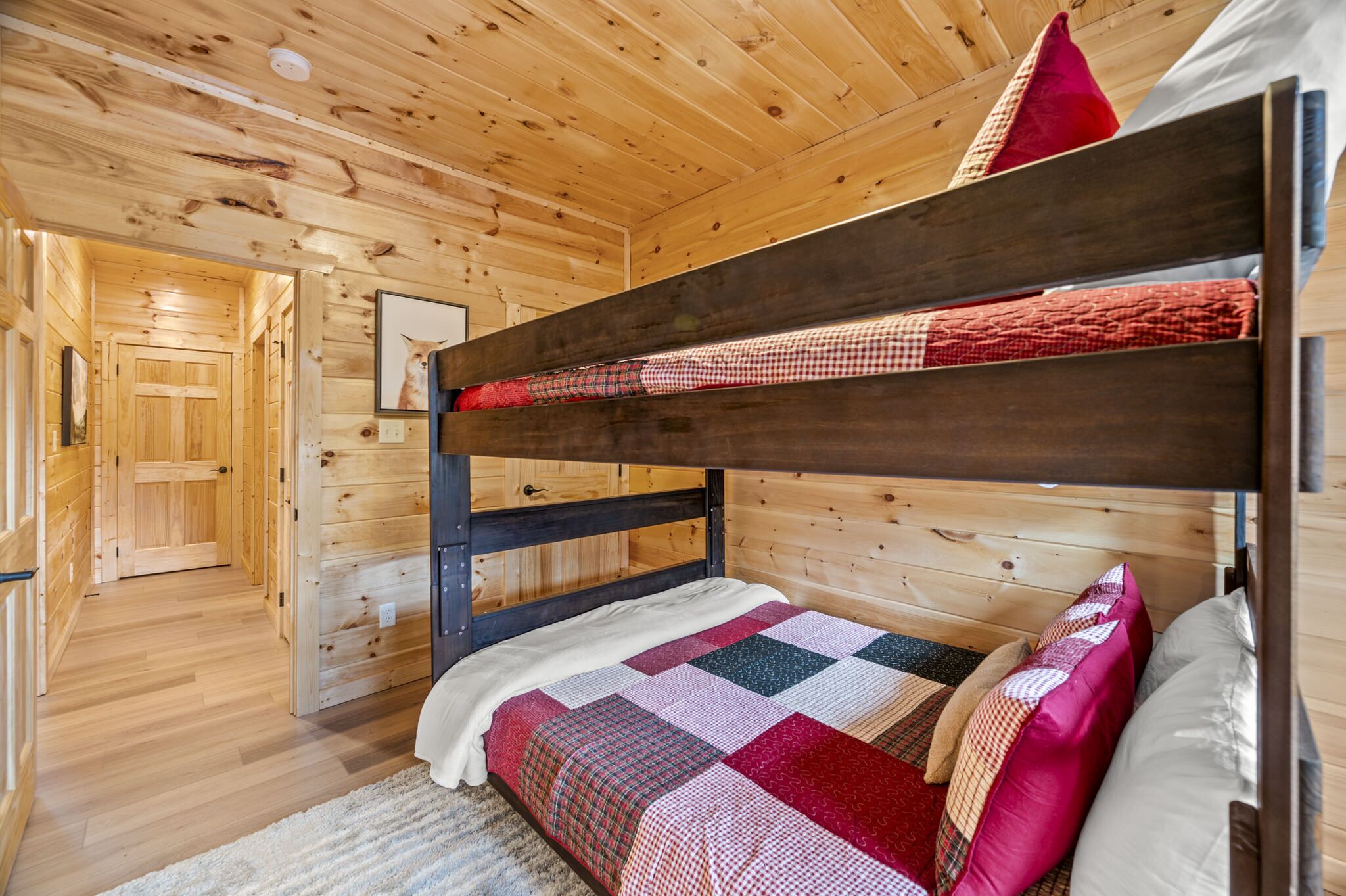 A bunk bed with a quilted bedspread and pillows, wooden walls, and a door leading to another room.