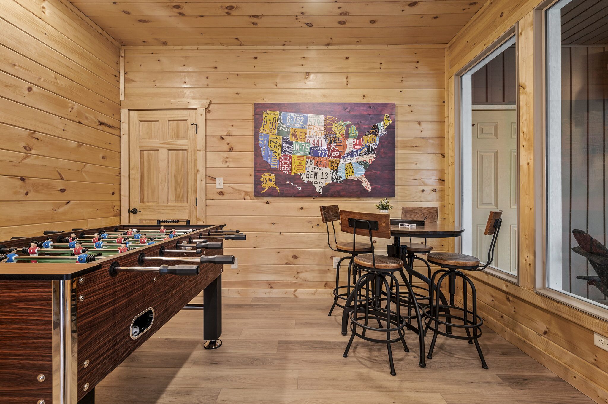 Ein Zimmer mit Holzboden, einer Tischkickeranlage, einem Essbereich mit Stühlen und einer großen Karte der USA an der Wand.