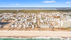 An aerial view of a coastal residential area with houses, a beach, and a bridge in the distance.