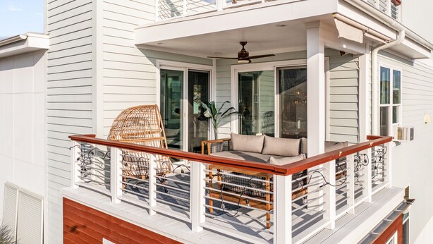 A two-story house with a balcony featuring wicker furniture and a wooden railing.