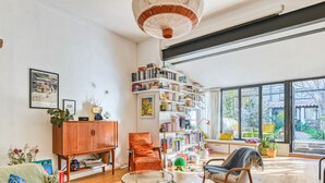 Un salón espacioso con una amplia estantería, un sofá cómodo, una mesa de centro de vidrio y vistas a un jardín a través de grandes ventanales.