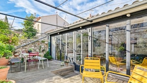 Un patio techado al aire libre con piso de madera, sillas amarillas y plantas en macetas.