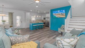 A modern living room with a large sofa, a coffee table, and a TV mounted on a teal accent wall. - New Beautiful Home @ Ocean Lakes Family  Campground! BE THE FIRST TO RENT! (Myrtle Beach)