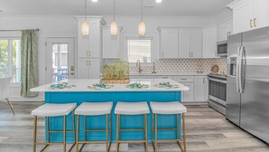 A modern kitchen with white cabinets, a central island with bar stools, a stainless steel refrigerator, and pendant lighting. - New Beautiful Home @ Ocean Lakes Family  Campground! BE THE FIRST TO RENT! (Myrtle Beach)