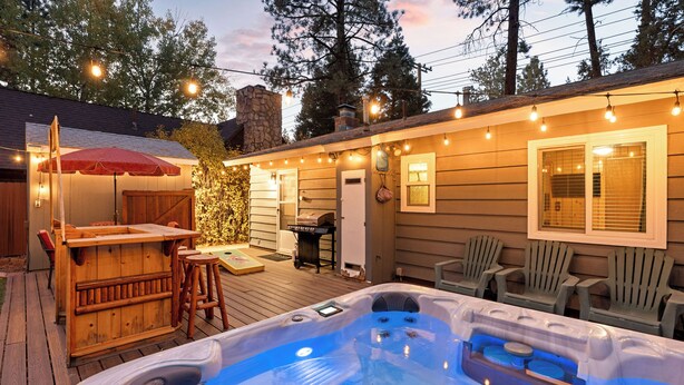 A hot tub with a wooden deck, outdoor seating, and string lights.