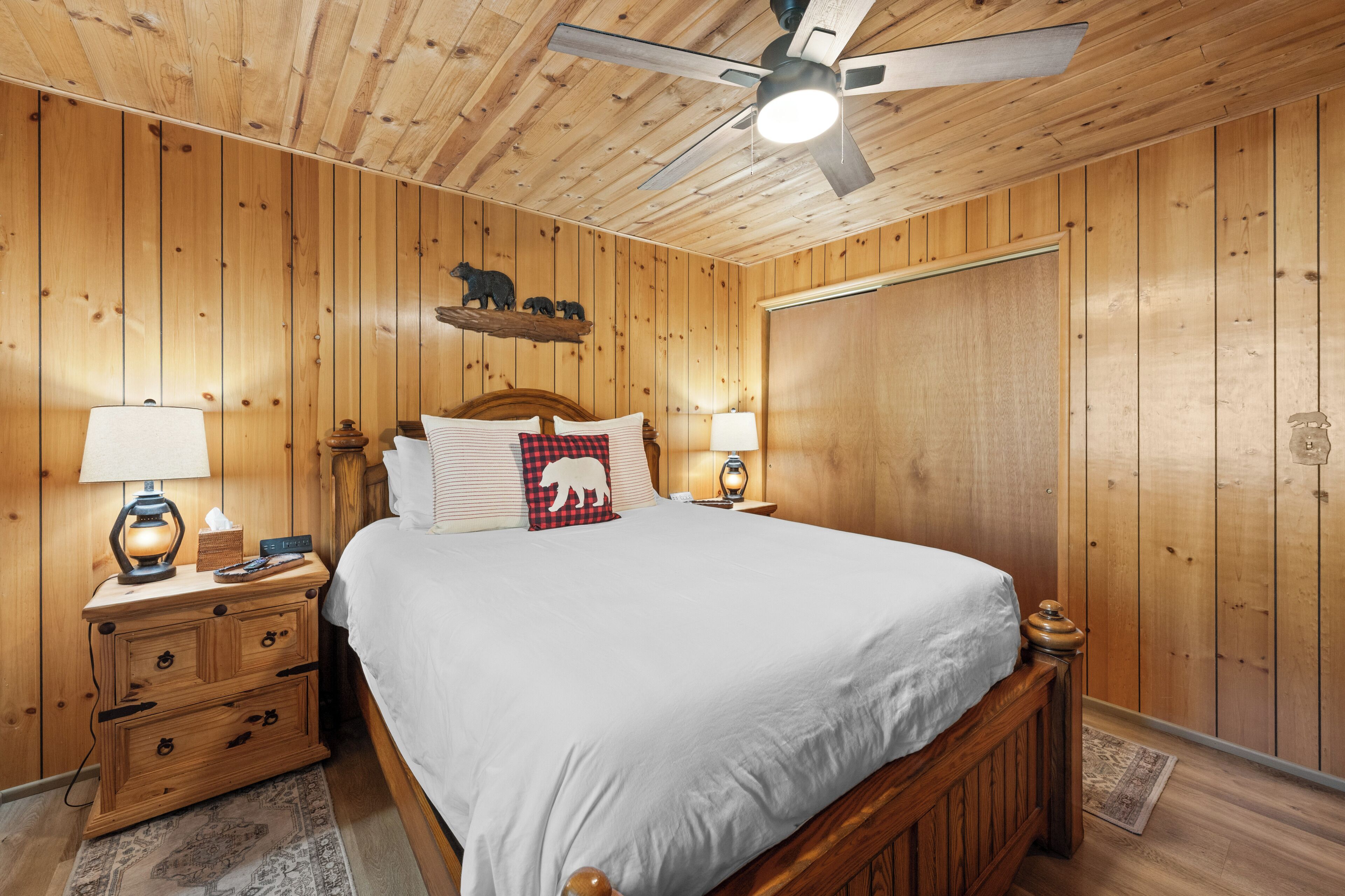 Ein Schlafzimmer mit Holzwandverkleidung, einem Bett, Nachttischen und einem Deckenventilator.