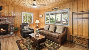 A cozy living room with a fireplace, leather sofa, and a ceiling fan.