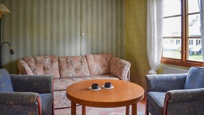 Un salon comprenant un canapé, deux fauteuils et une table ronde en bois sur laquelle sont posées deux bougies.