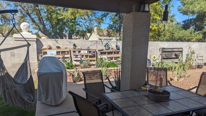 Una veranda esterna con tavolo e sedie, una poltrona sospesa e un muro decorativo con diversi oggetti.