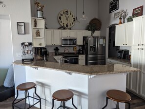A kitchen with white cabinets, a granite countertop, a stainless steel refrigerator, and a clock.