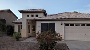 Una casa residenziale con tetto in tegole, un garage e un piccolo giardino con fiori rossi.